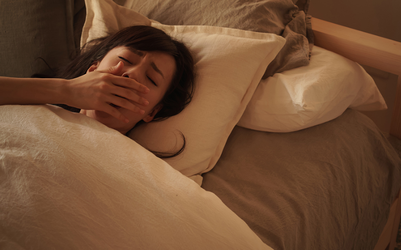 女性がベッドの中であくびをしている写真